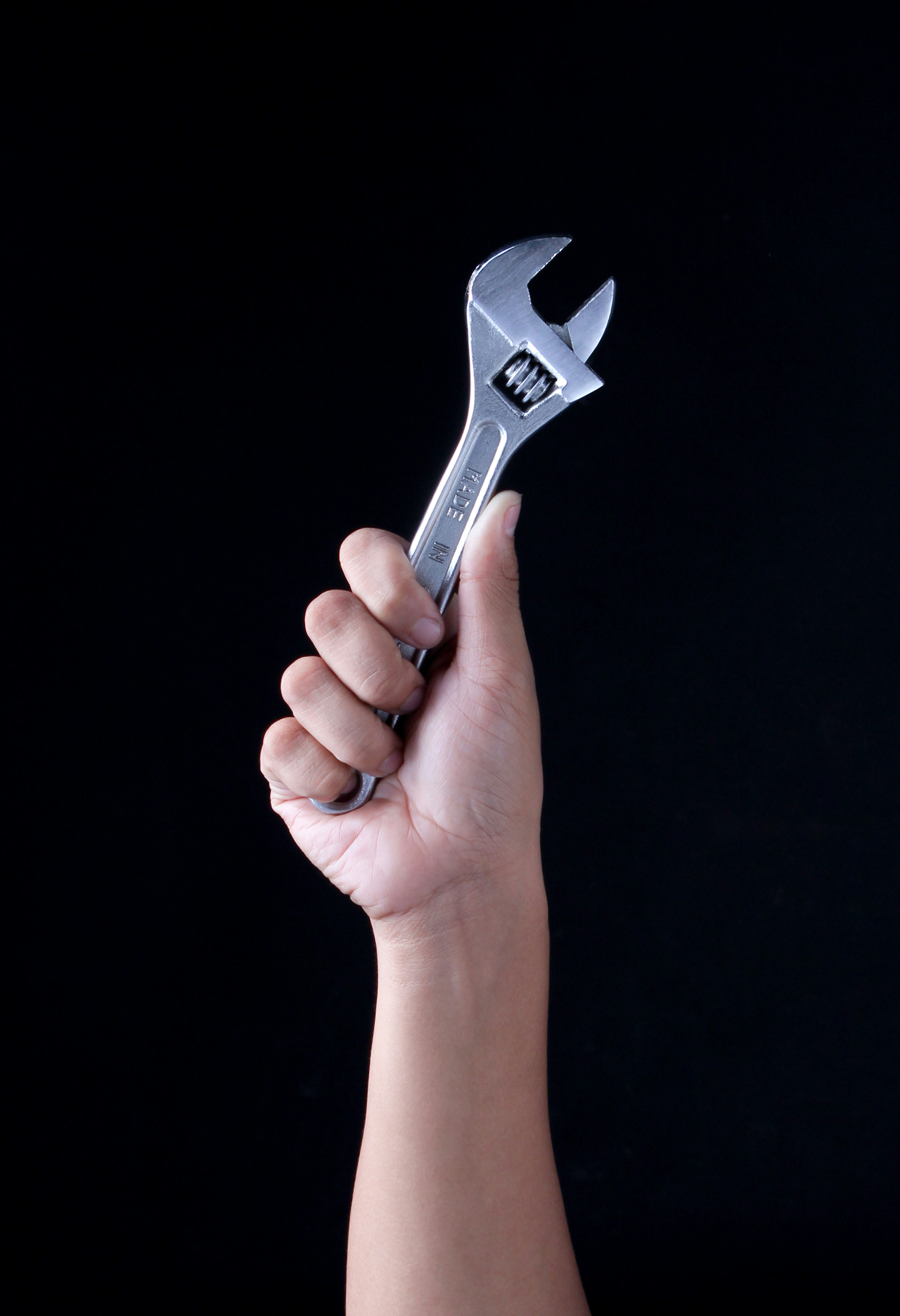 A hand holding an adjustable wrench against a black background